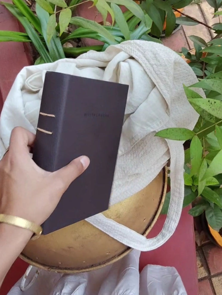 Person holding a dark brown leather feel journal with plants in the background